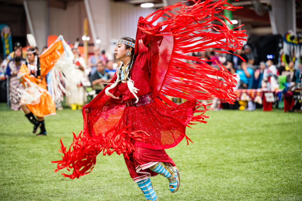 Native American woman in vibrant red fringe regalia dancing at the Alabama-Coushatta 56th Annual Powwow in Texas
