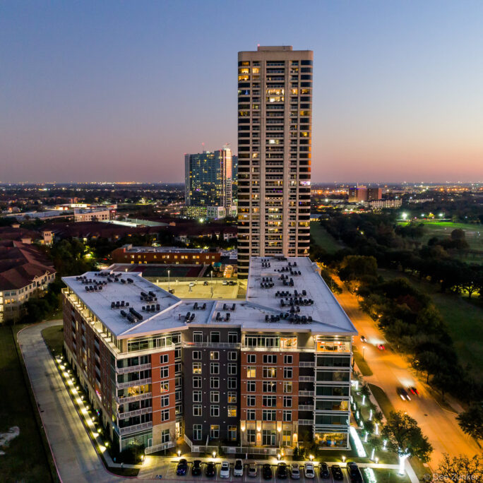 Aerial drone photo of a high-rise apartment complex near Hermann Park in Houston, TX, captured glowing at twilight.