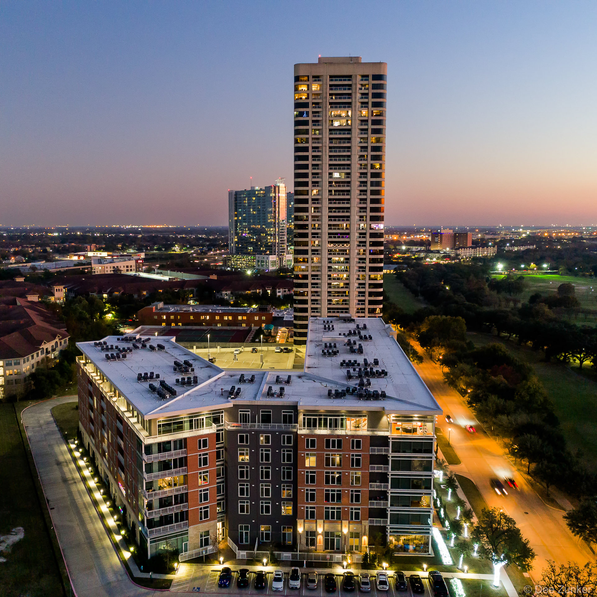Aerial drone photo of a high-rise apartment complex near Hermann Park in Houston, TX, captured glowing at twilight.