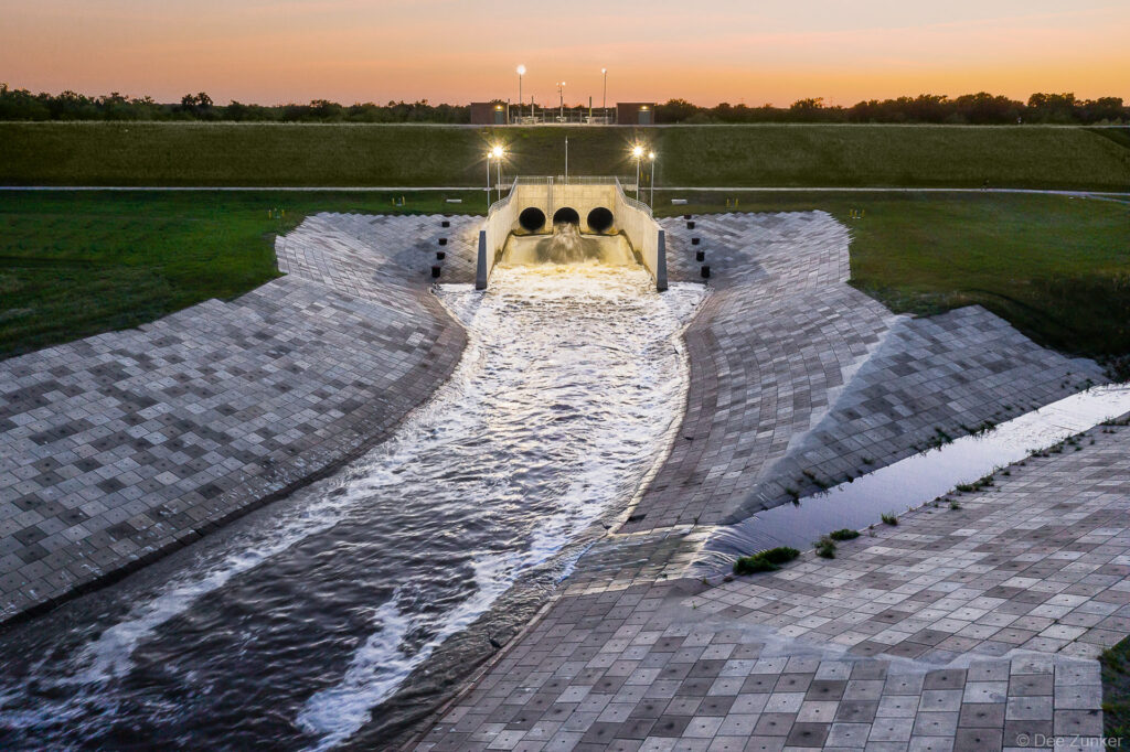 Aerial drone photo of the Barker Reservoir spillway. Glowing lights illuminate the water infrastructure as the sun sets at twilight.