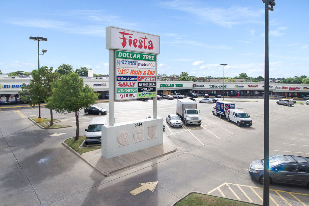 Drone aerial view of Fiesta grocery strip mall at 5334 in Dallas TX showing parking lot and tenant signage including Dollar Tree and Wing Stop.