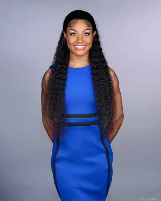 Houston professional woman in blue sleeveless dress poses for corporate studio headshot against gray background.