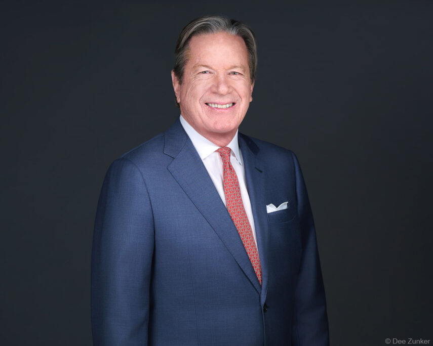 Senior male executive in navy suit and red tie poses for a professional corporate headshot against a dark gray studio background in Houston.