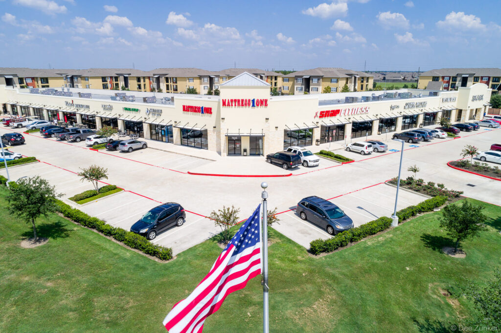 Aerial drone photo of a retail strip mall at 7035 West Grand Parkway South featuring Mattress One and Snap Fitness, Houston TX.