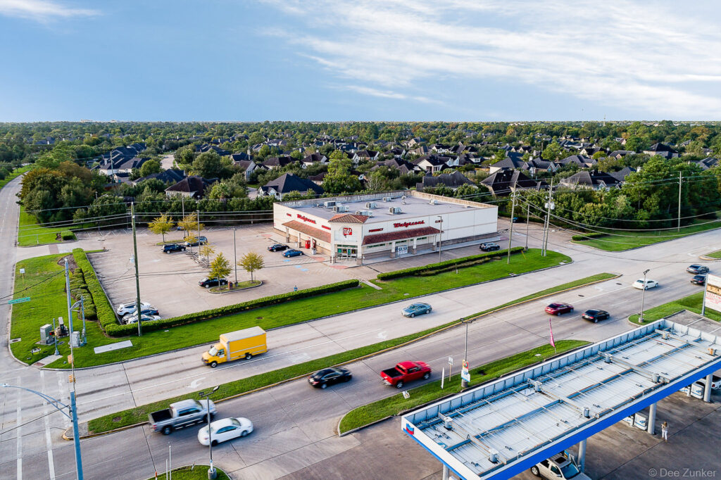 Aerial drone photo of Walgreens pharmacy at busy Cypress TX intersection, with suburban neighborhood and Chevron gas station visible.