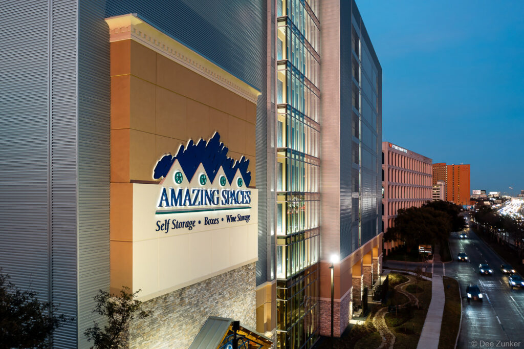 Aerial dusk view of Amazing Spaces Self Storage multi-story building near Greenway Plaza, Houston, with illuminated signage and freeway.
