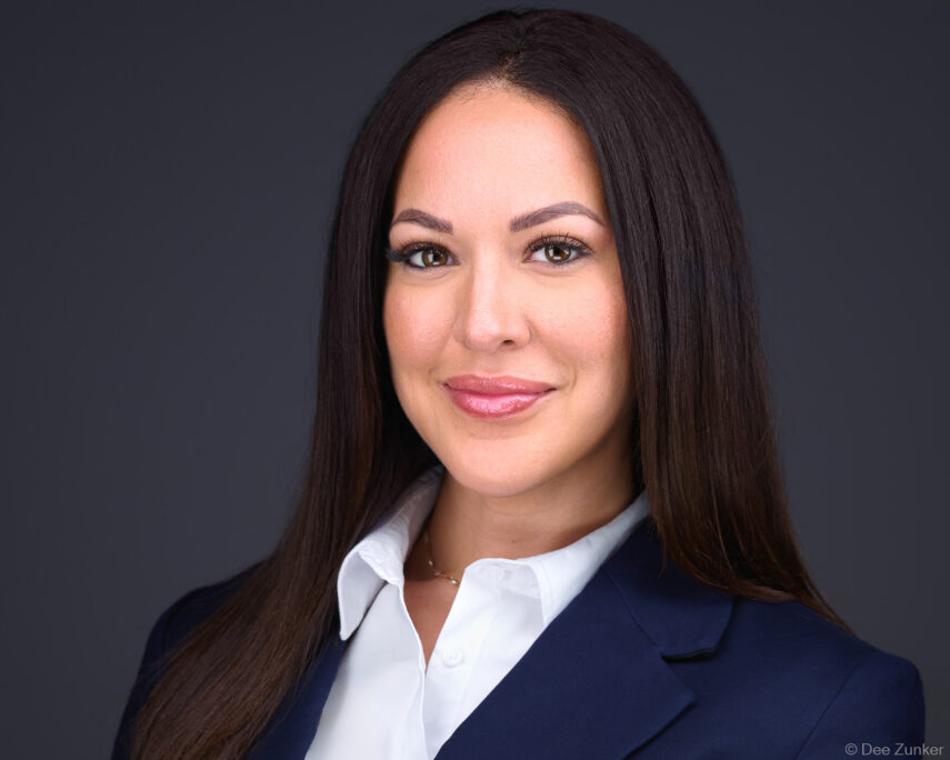 Houston attorney professional headshot, woman in navy blazer and white blouse against gray studio background, corporate portrait photography.