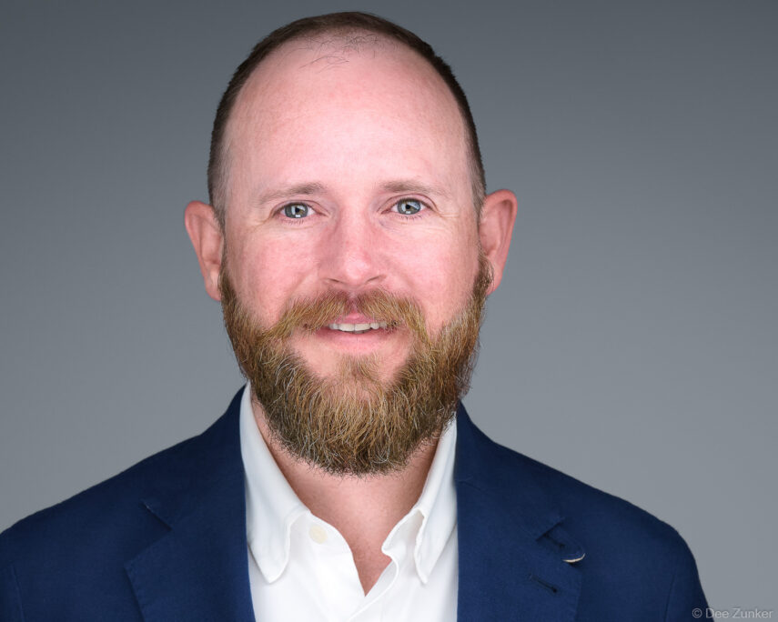 Male construction executive with beard and blue blazer poses for a professional studio corporate headshot against a gray background in Houston.