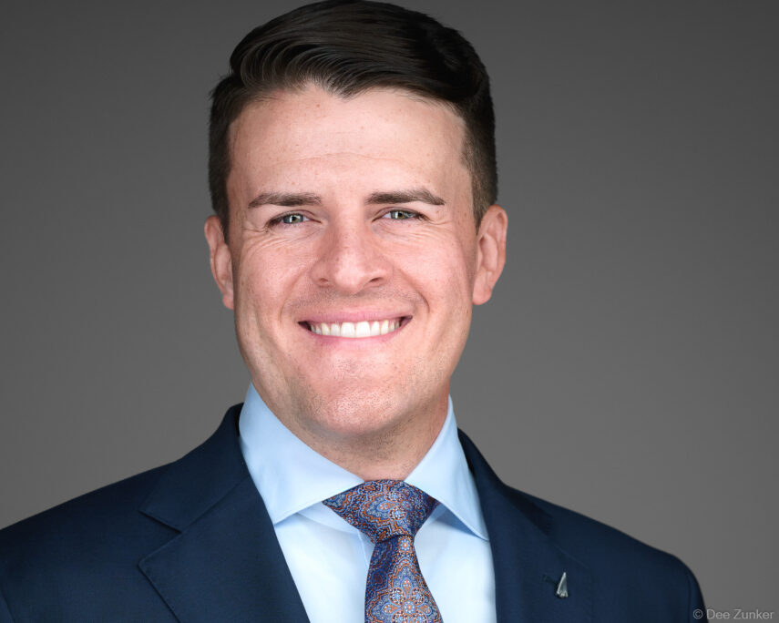 Male attorney in navy suit and paisley tie poses for a professional corporate headshot against a gray studio background in Houston.