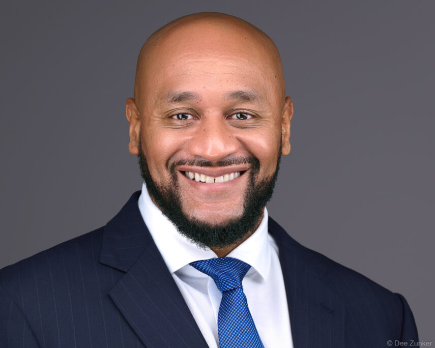 Smiling bald man with beard in navy pinstripe suit and blue tie, professional studio headshot on gray background, Houston.