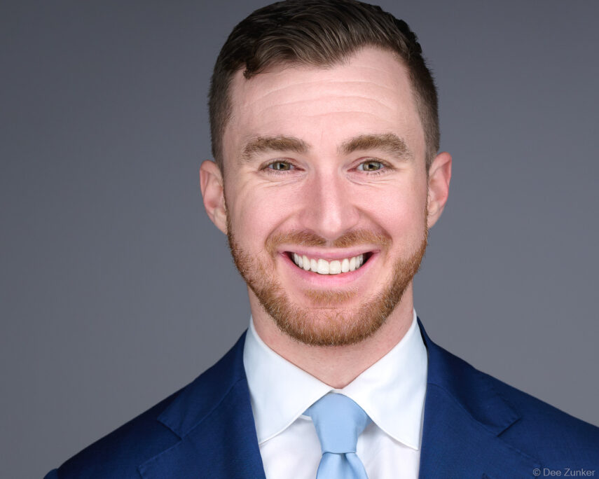 Professional male corporate headshot on gray background, navy suit and light blue tie, studio photography by Houston commercial photographer.