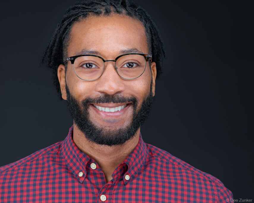 Smiling male professional in red plaid shirt and glasses, studio corporate headshot on dark background, Houston commercial photography.