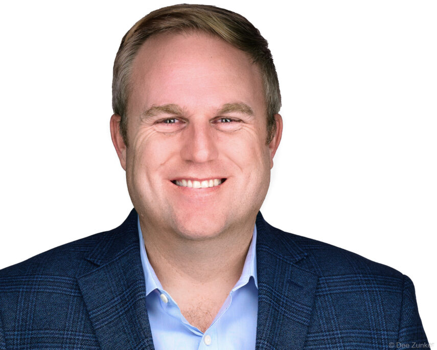 Male corporate professional in navy blazer and light blue shirt, smiling, white background studio headshot, Houston, TX.