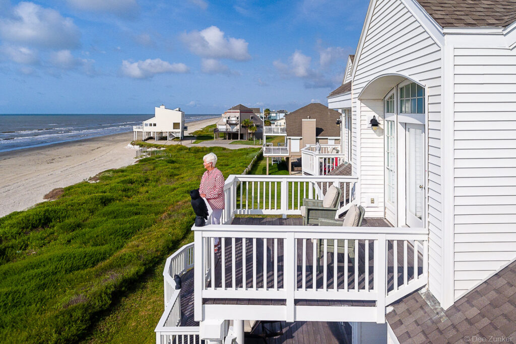 Aerial drone photo of a woman on a white beachfront condo deck overlooking the Gulf of Mexico in Galveston TX