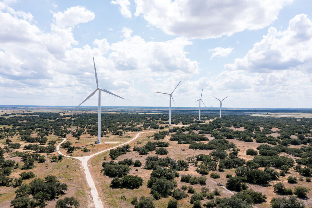 Drone aerial photo of Rattlesnake Wind Farm turbines rising above sparse Texas scrubland with winding dirt access roads.
