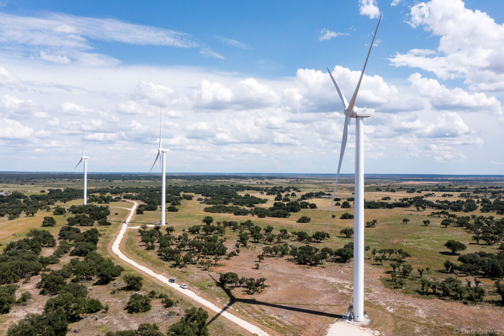 Drone aerial photo of Rattlesnake Wind Farm turbines across West Texas scrubland with access road and partly cloudy sky.