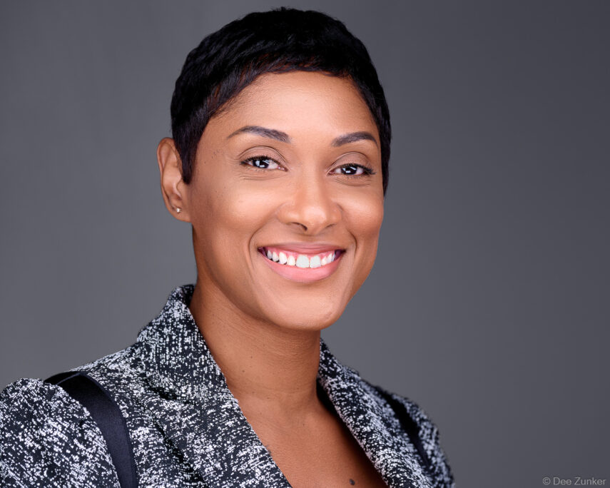 Professional corporate headshot of a smiling woman with short hair wearing a speckled blazer against a gray studio background in Houston.