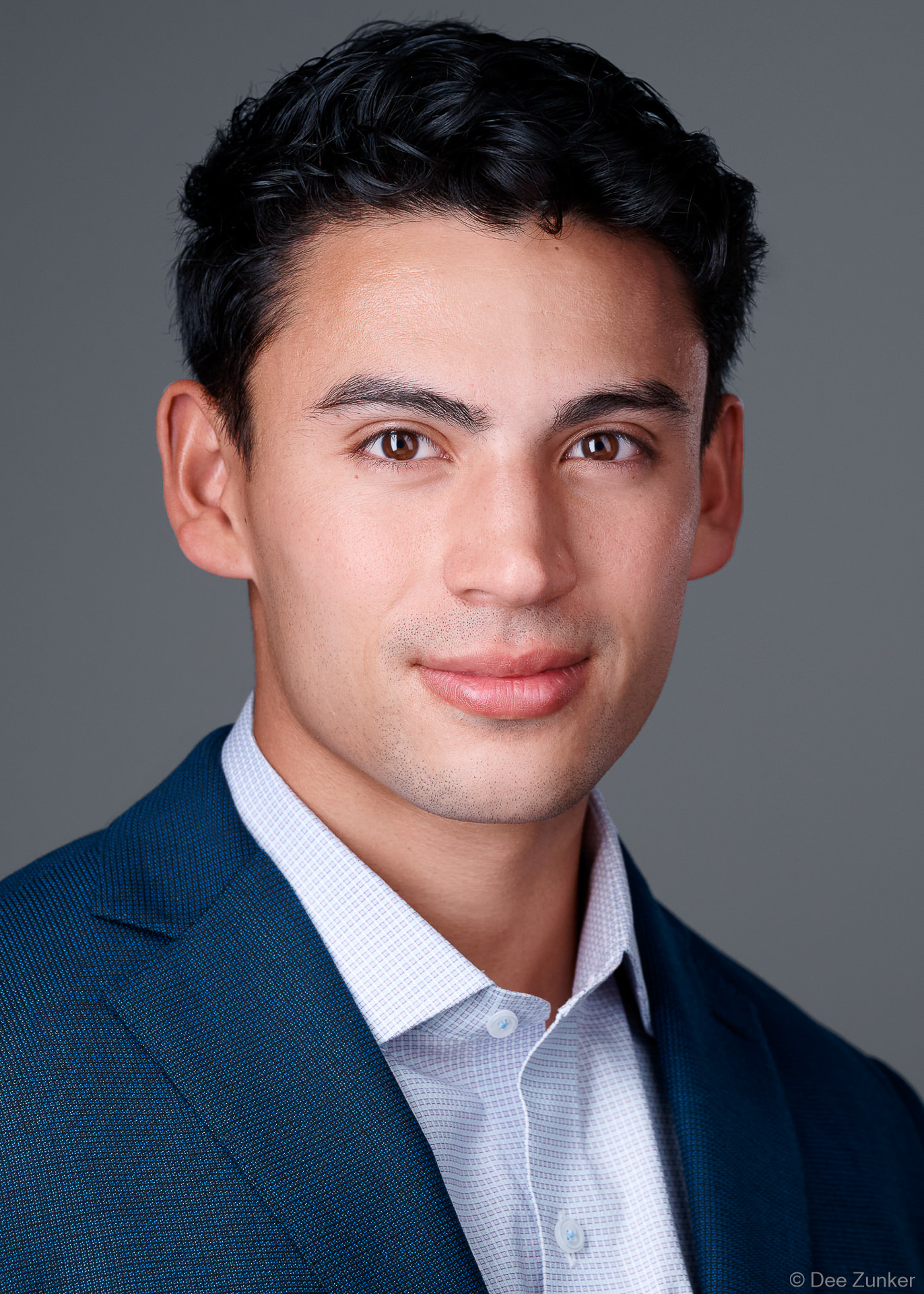 ERAS residency application headshot of a young male medical professional in navy blazer, shot in 5x7 format near Texas Medical Center, Houston with medium gray background.