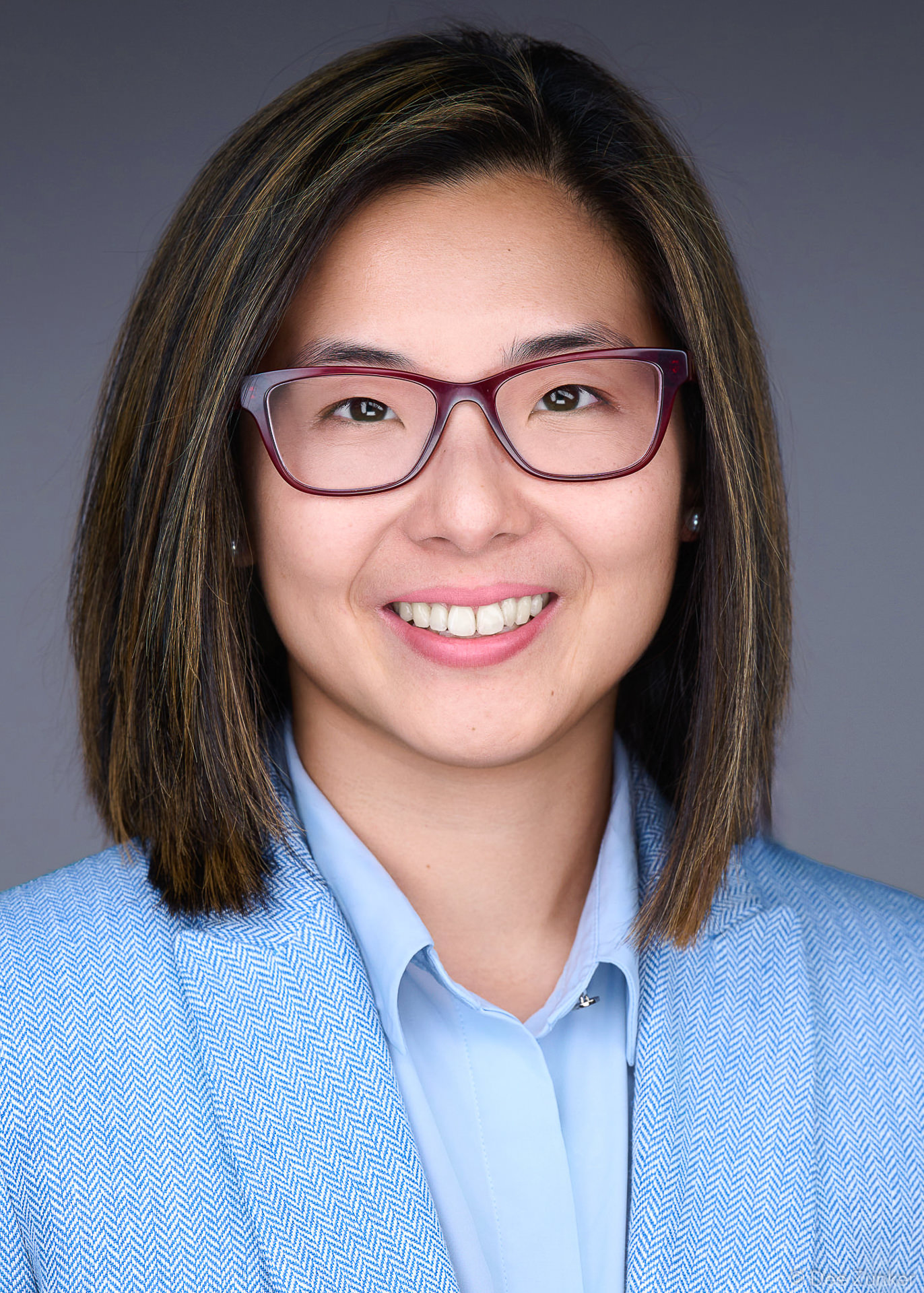 ERAS residency applicant headshot, 5x7 format, smiling woman with glasses in blue blazer, professional corporate portrait near Texas Medical Center Houston TX with dark blue gray background