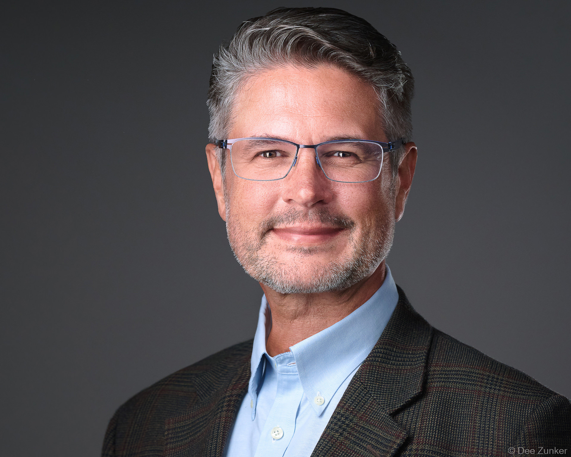 Professional male executive studio headshot, gray background, dark blazer and light blue shirt, glasses, Houston corporate photography.