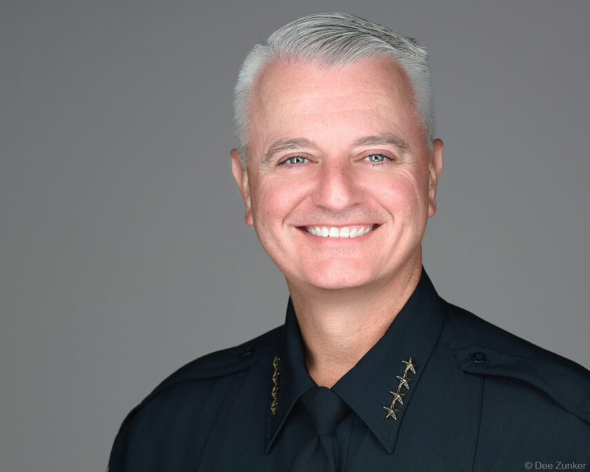 Male executive in dark uniform with gold stars smiles in a professional studio headshot against a gray background in Houston.