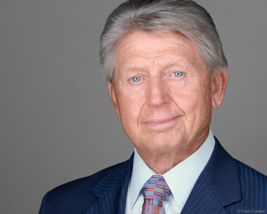 Senior male executive with gray hair and blue eyes in navy suit, professional studio headshot on gray background, Houston corporate photography.