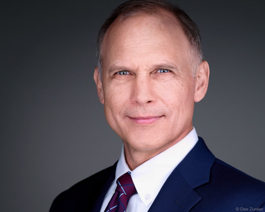 Male executive in navy suit and burgundy tie poses for a professional corporate headshot against a gray studio background in Houston.