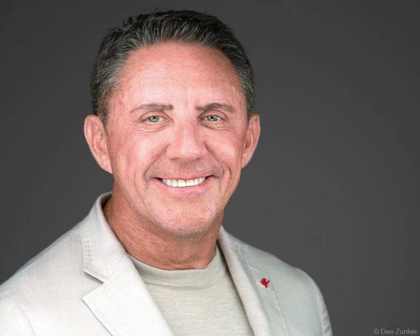 Smiling male executive in white blazer poses for professional corporate headshot against neutral gray studio background in Houston.