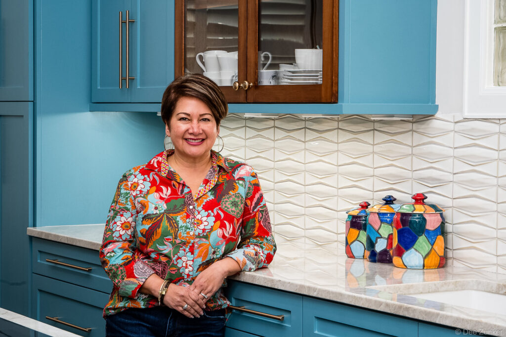 Woman in floral shirt leaning against marble countertop in teal blue kitchen, Richton home interior branding photography
