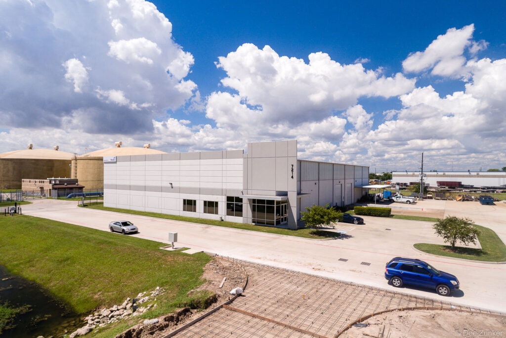 Drone aerial view of Harms Business Park Houston showing modern industrial warehouse building with adjacent storage tanks and parking lot.