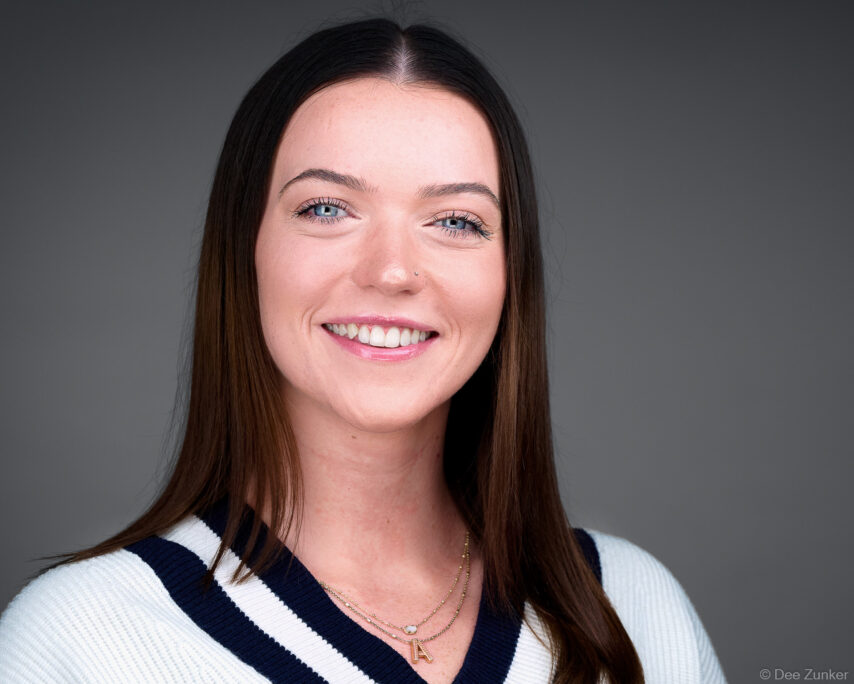 Smiling healthcare professional with blue eyes and dark hair poses for a studio corporate headshot against a gray background in Houston, TX.