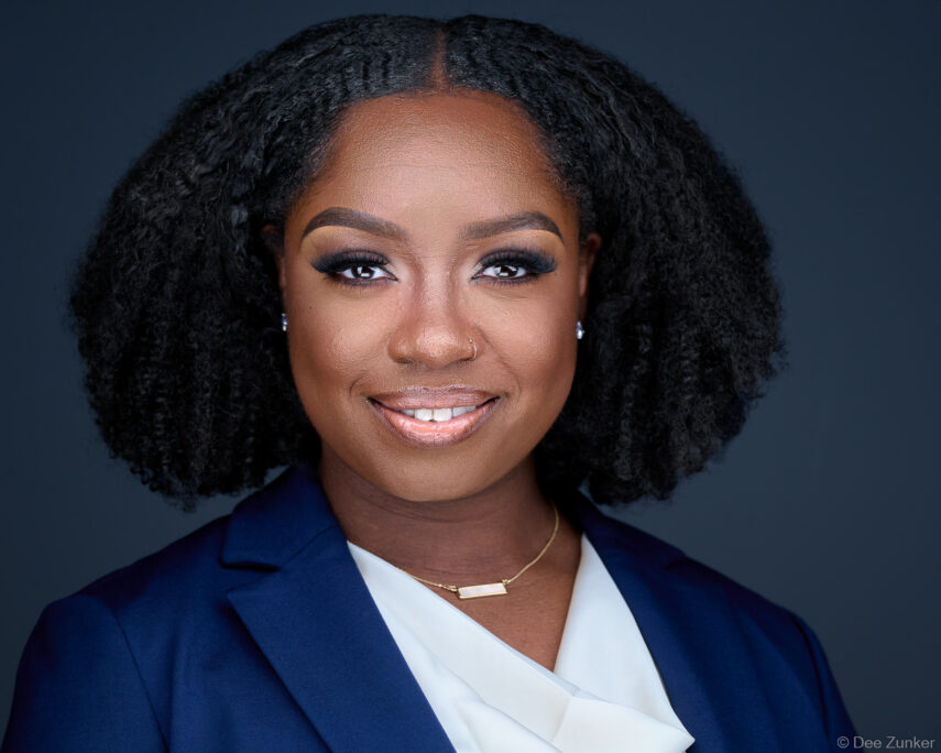 Professional corporate headshot of a Houston attorney in a navy blazer and white blouse, smiling confidently against a dark studio background.
