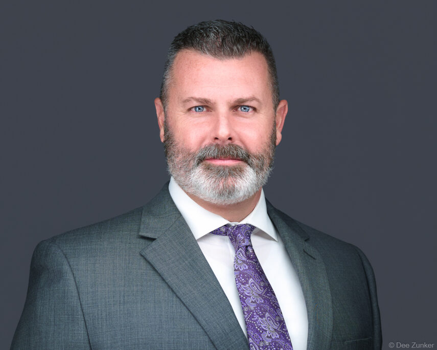 Male Houston attorney in gray suit and purple paisley tie poses for a professional corporate headshot against a gray studio background.