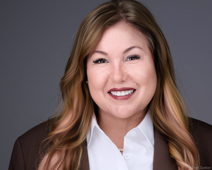 Professional corporate headshot of a Houston attorney, smiling, wearing a dark blazer and white shirt, photographed against a gray studio background.