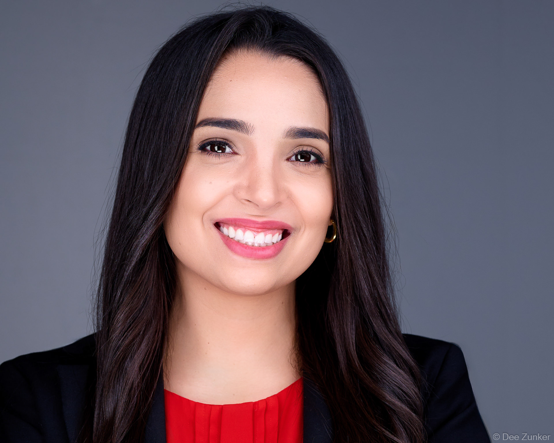 Professional corporate headshot of a female attorney in a black blazer and red top, photographed in a Houston studio against a gray background.