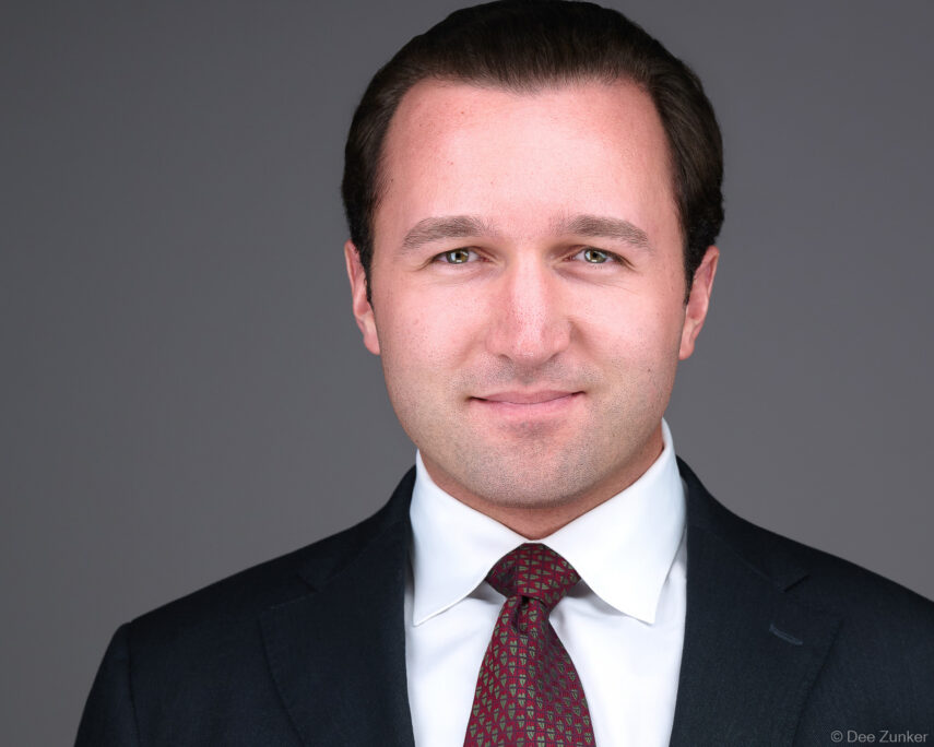 Male attorney professional headshot on gray background, studio portrait by Houston corporate photographer, dark suit and burgundy tie.