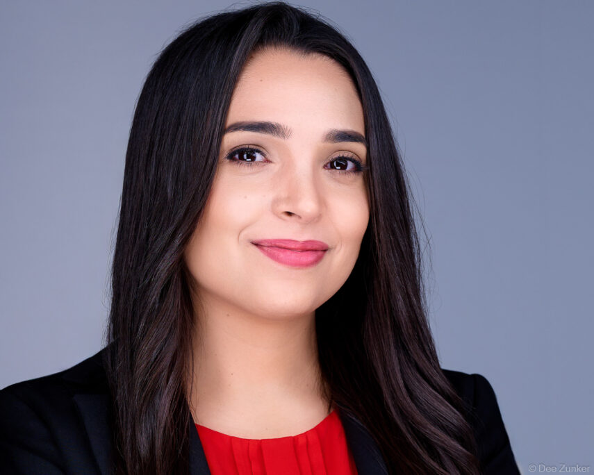 Professional corporate headshot of a female attorney in a black blazer and red top, studio portrait with gray background, Houston, TX.
