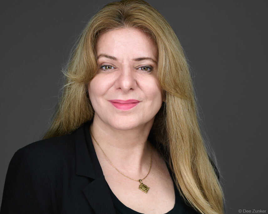 Female attorney with blonde hair and gold necklace poses for a professional corporate studio headshot against a gray background in Houston.