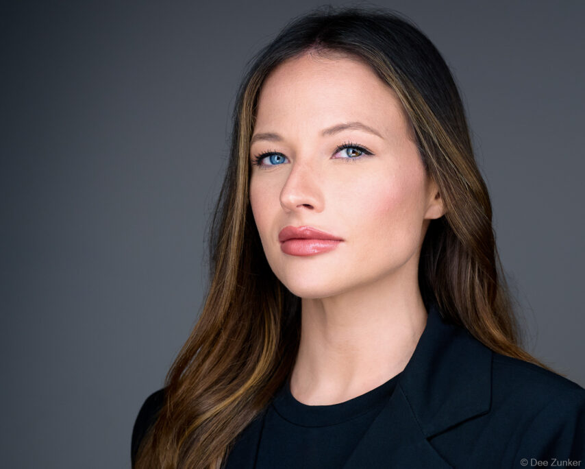 Studio corporate headshot of a female attorney with heterochromia, long brunette hair, and dark blazer against a gray background, Houston TX