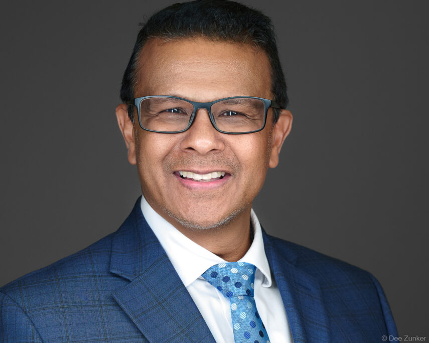 Male executive in blue plaid suit and blue tie smiles in professional studio headshot against gray background, Houston TX.