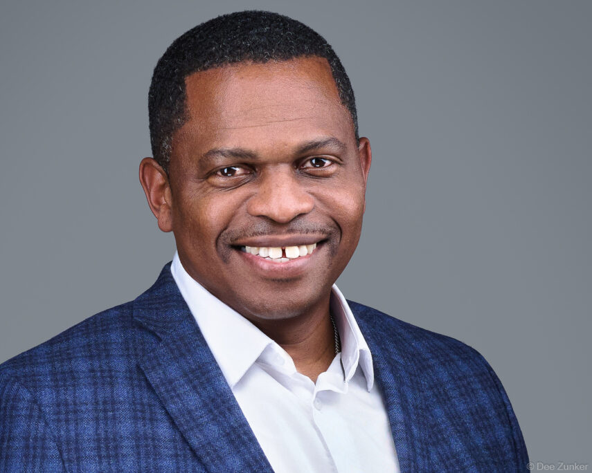 Professional corporate headshot of a smiling male executive in a blue blazer and white shirt against a gray studio background, Houston TX.