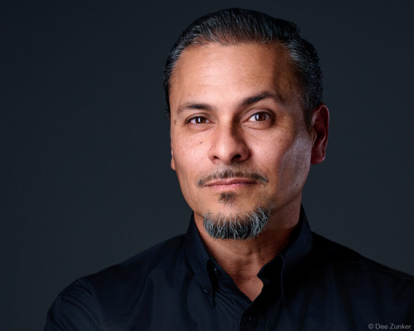 Professional studio headshot of a middle-aged Hispanic male executive, dark background, black shirt, Houston commercial photography.