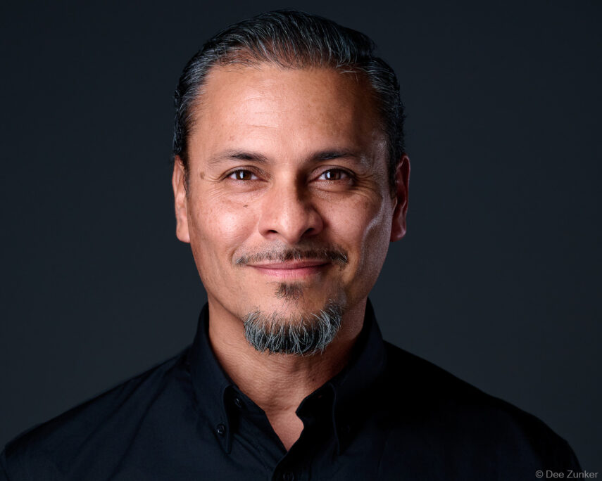 Professional male executive studio headshot, dark background, slicked-back hair and goatee, black shirt, shot in Houston by Dee Zunker Photography.