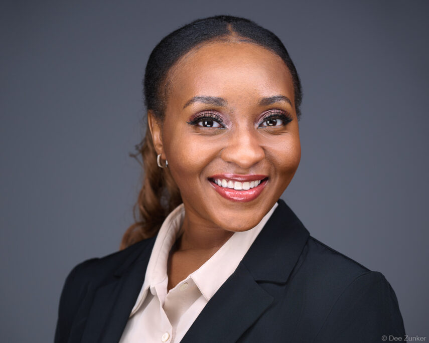 Professional woman in black blazer smiles in a Houston studio corporate headshot against a gray background, styled for business use.