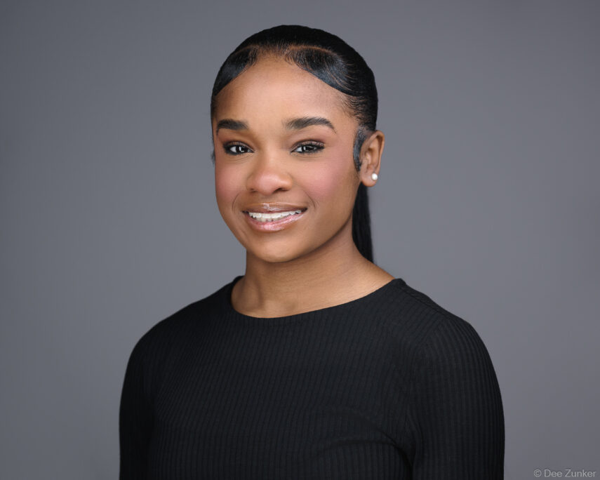 Professional studio headshot of a young woman in a black ribbed top against a gray background, captured by Houston corporate photographer.