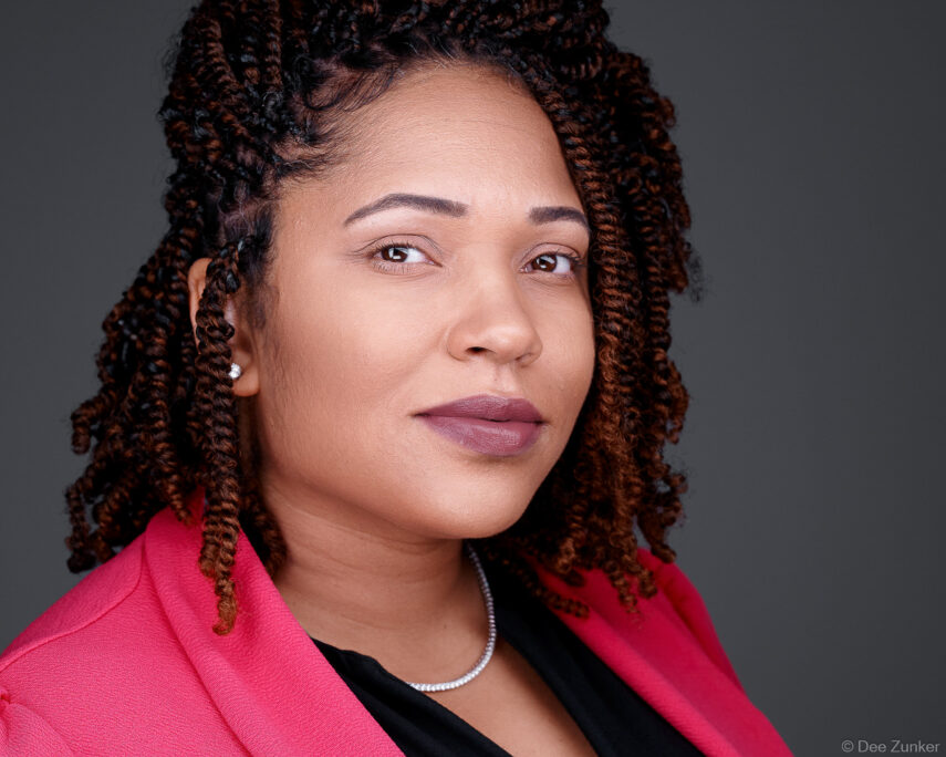 Professional corporate headshot of a woman in a pink blazer with twisted locs, studio portrait suitable for executive profiles and annual reports, Houston TX.