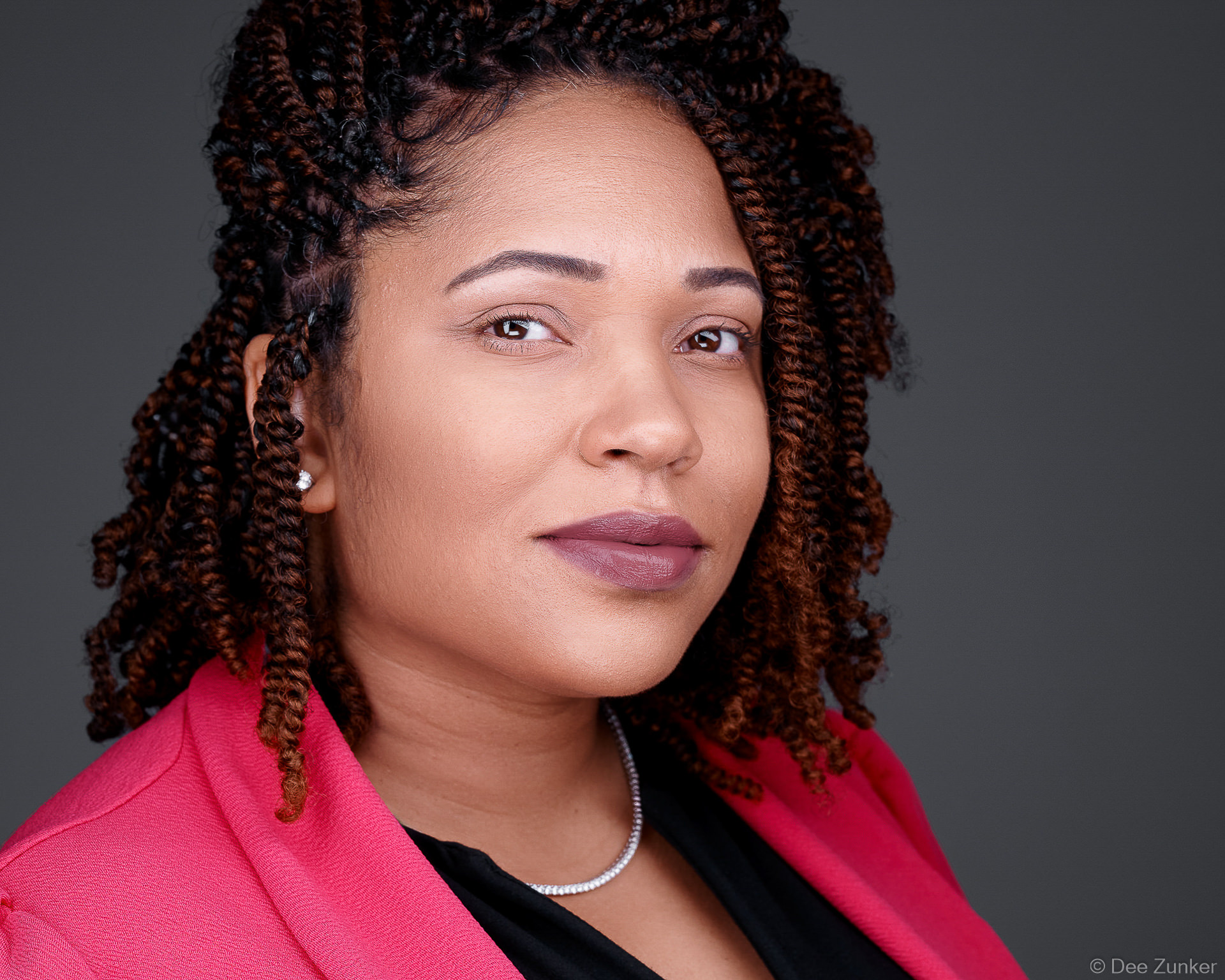 Professional corporate headshot of a woman in a pink blazer with twisted locs, studio portrait suitable for executive profiles and annual reports, Houston TX.