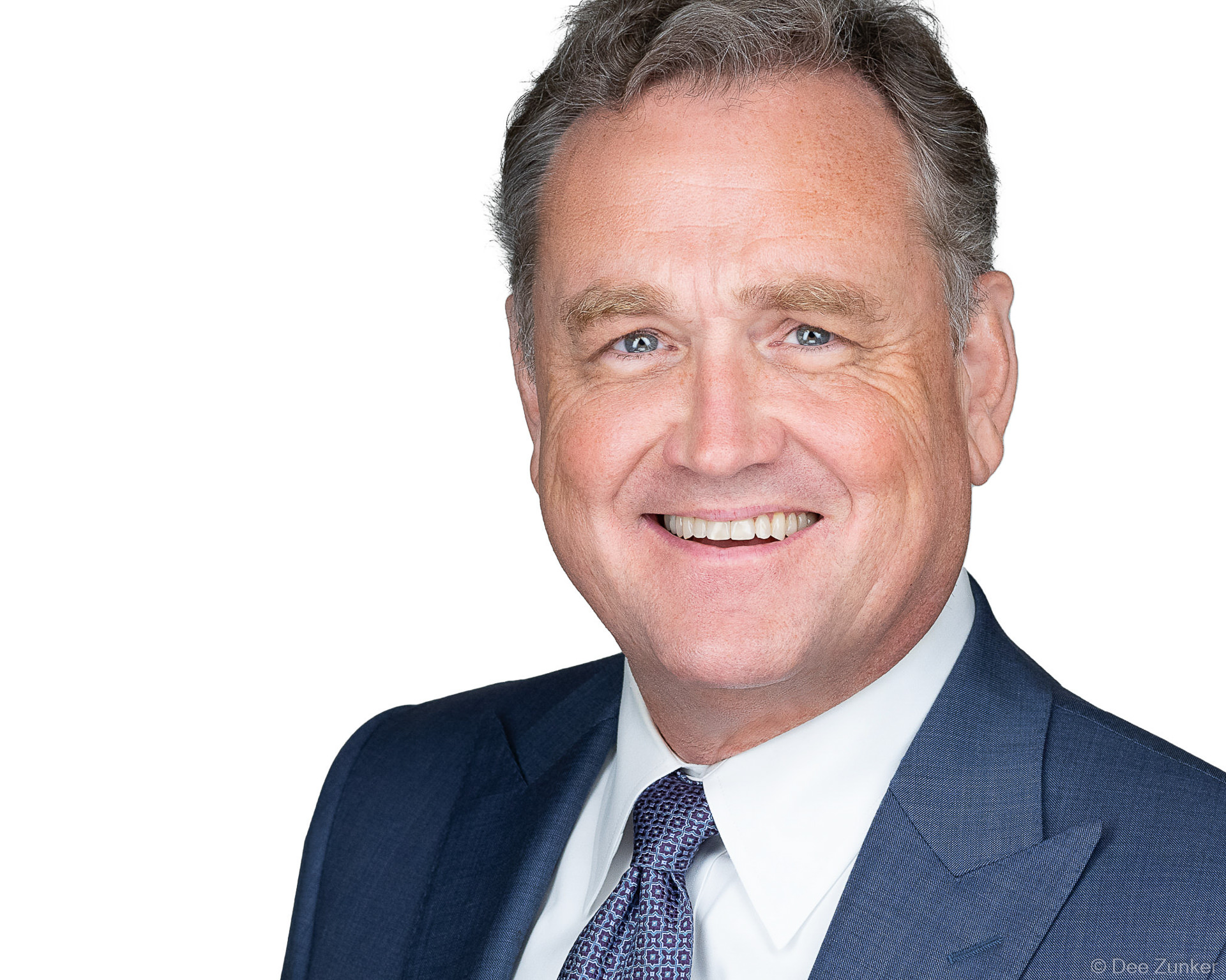 Professional male executive corporate headshot in navy suit and patterned tie, smiling confidently, ideal for annual reports or staff directories.