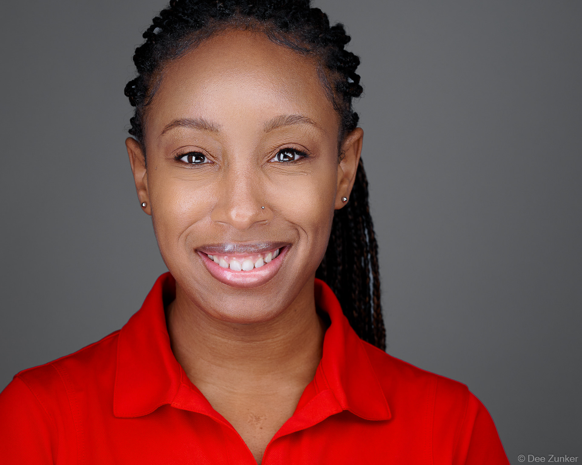Smiling Houston healthcare professional in red polo shirt, studio corporate headshot with gray background, captured by Dee Zunker Photography.