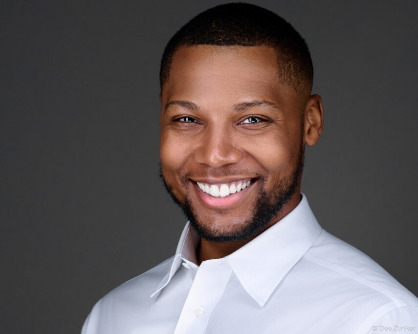 Professional corporate headshot of a smiling man in a white dress shirt against a gray studio background, Houston TX.